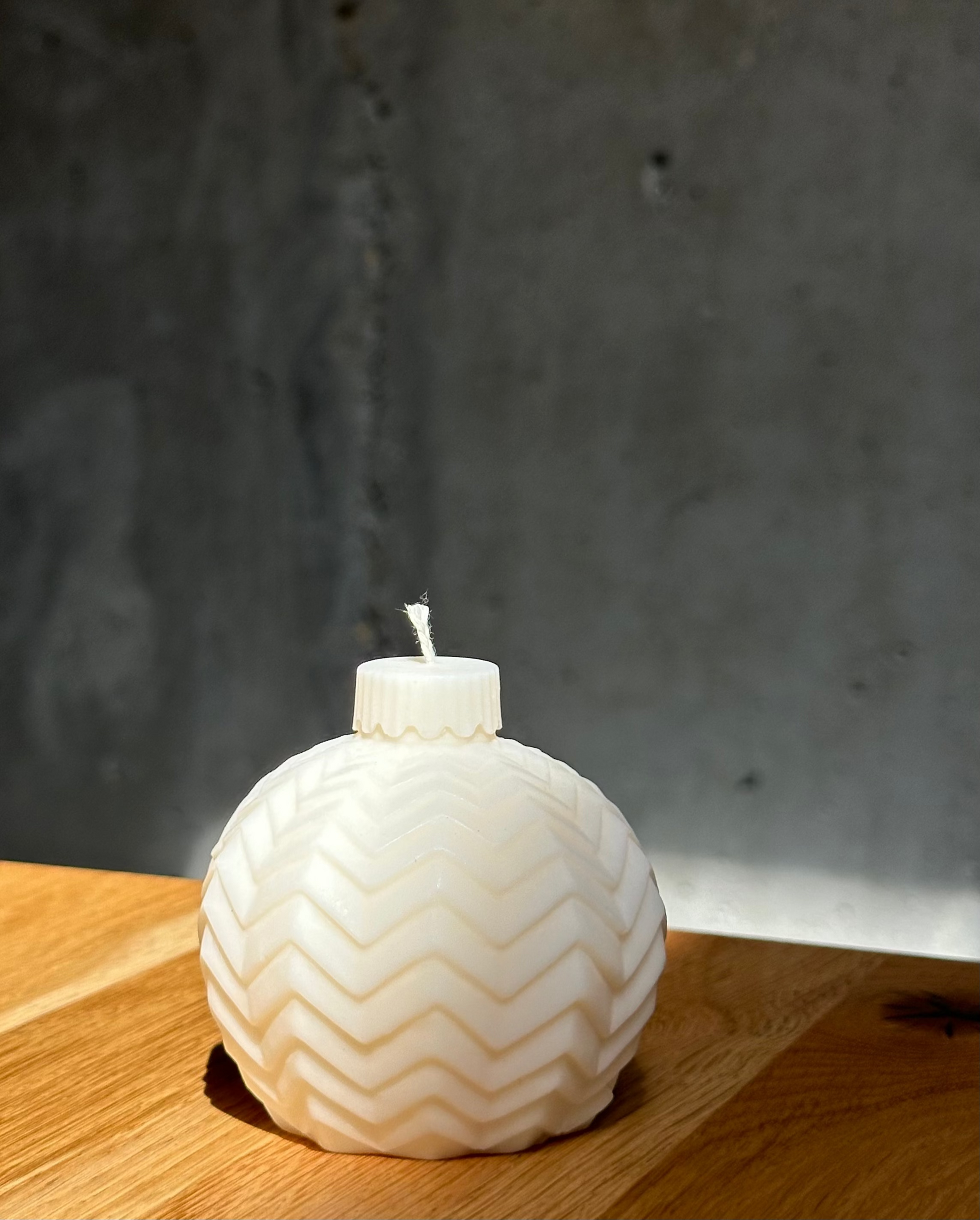 White candle with a zigzag pattern on a wooden surface against a dark background