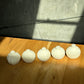 Five white soy candles items arranged on a wooden surface with a concrete wall in the background.