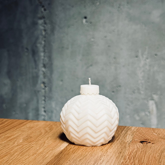 White soy candle holder with a candle on a wooden surface against a gray concrete wall.