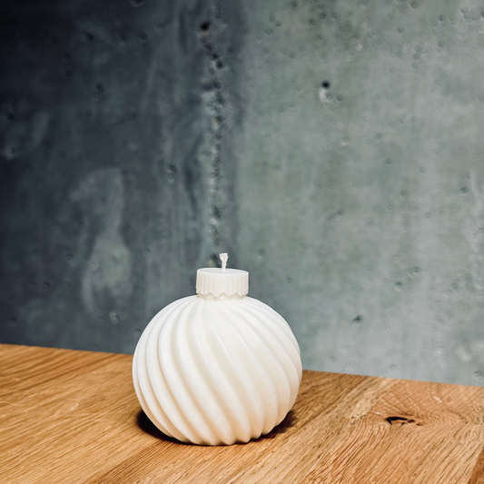 White ribbed candle  on a wooden surface with a gray concrete wall background